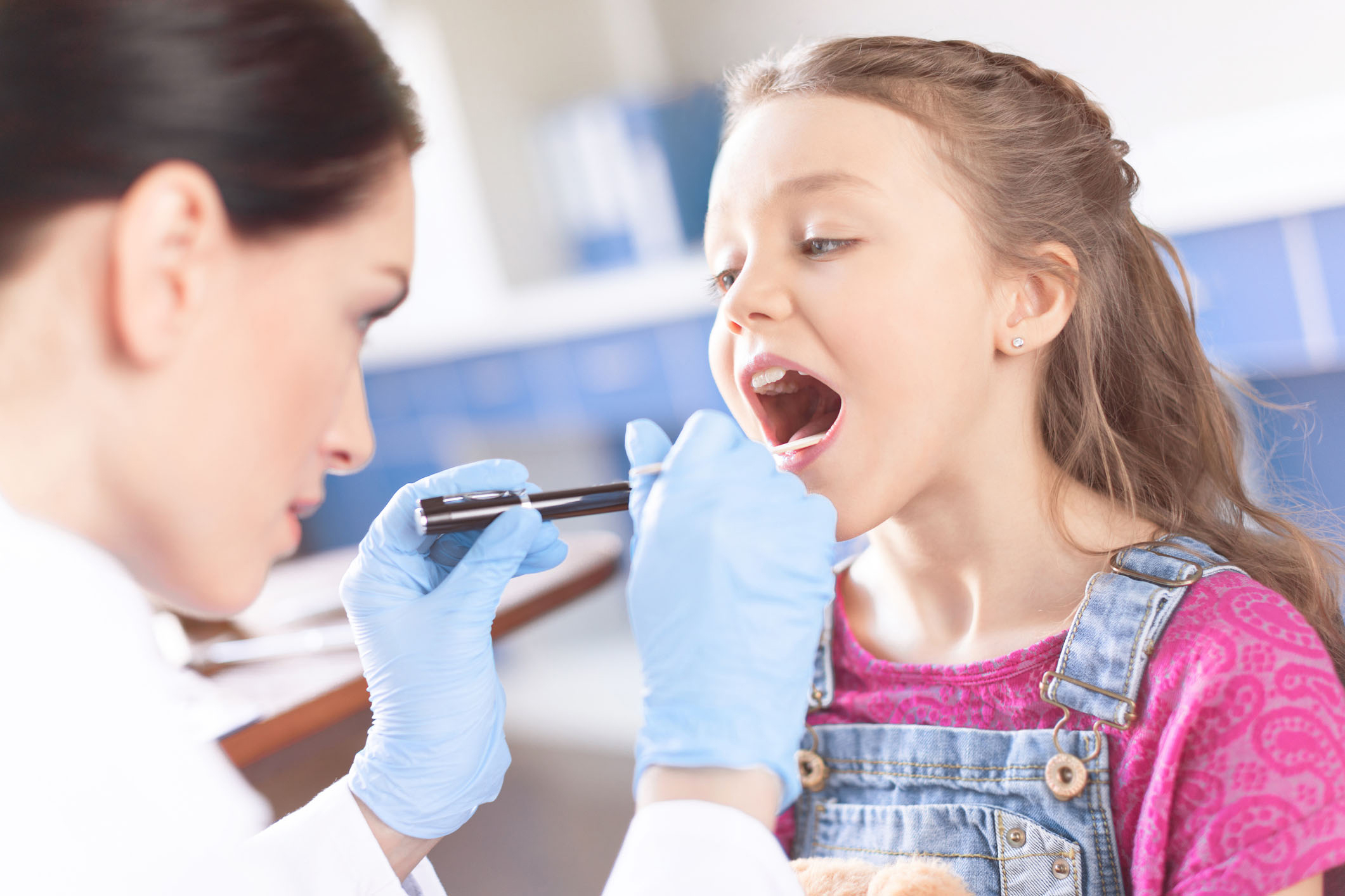 Woman doctor examining a girls throat with a spatula and flashlight