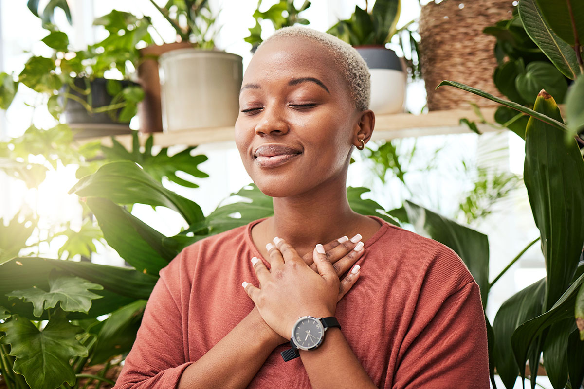 Young black woman meditating among plants indoors.